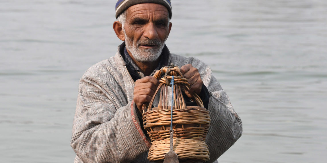 ٹھٹھرتی سردی کے بیچ جھیل ڈل میں معمر شہری کانگڑی سے گرمی کرتے ہوئے۔۔۔۔(فوٹو :ساحل میر)